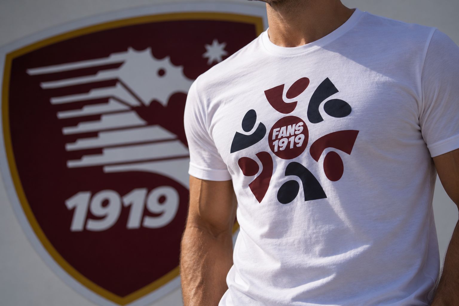 Un tifoso con la maglia FANS 1919 davanti allo stemma della Salernitana